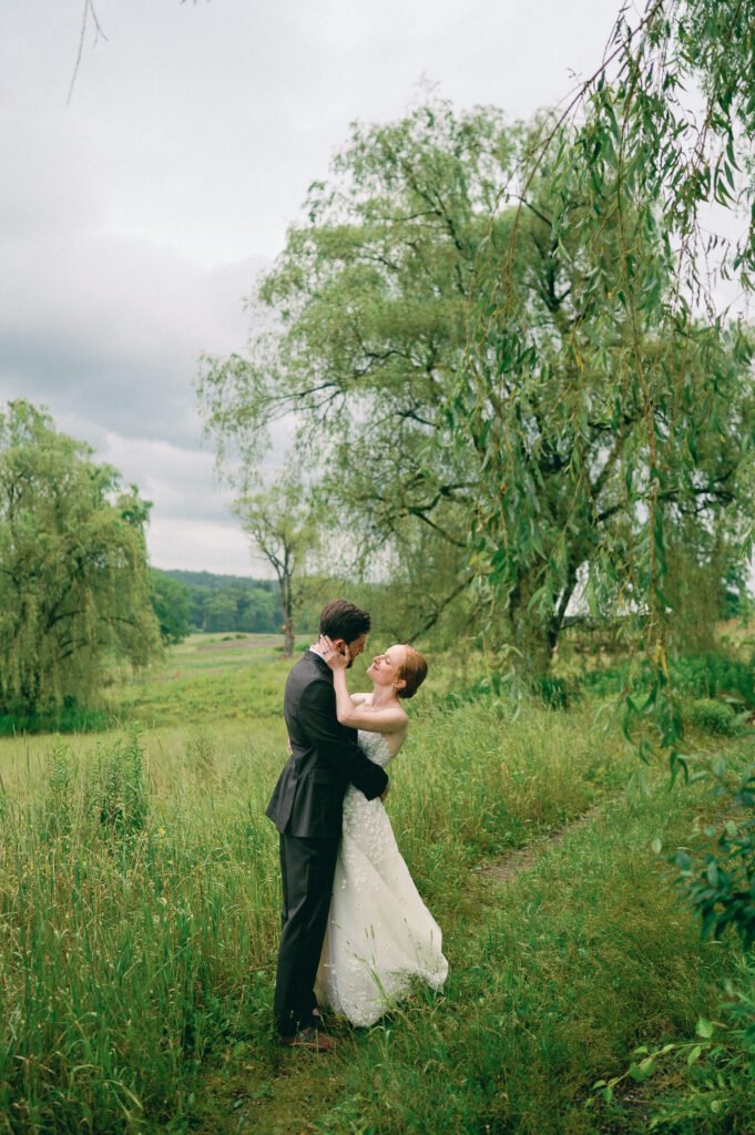 Couple standing in a field with a weeping willow in the background at Inness
